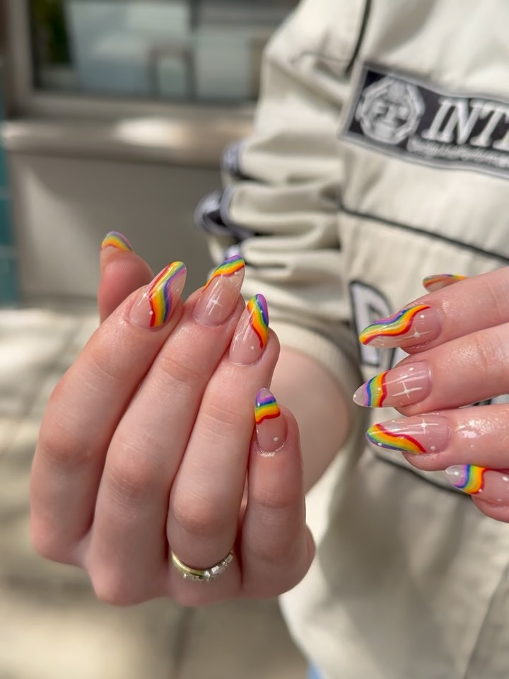Rainbow Pride-themed nail art on sheer French tip nails